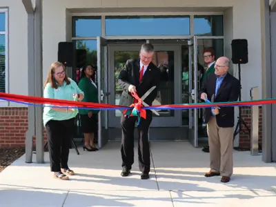University, 4-H and FFA representatives cut red, blue and green ribbons outside the entrance of the new CALS Extension Building as North Carolina 4-H and FFA state officers hold them.