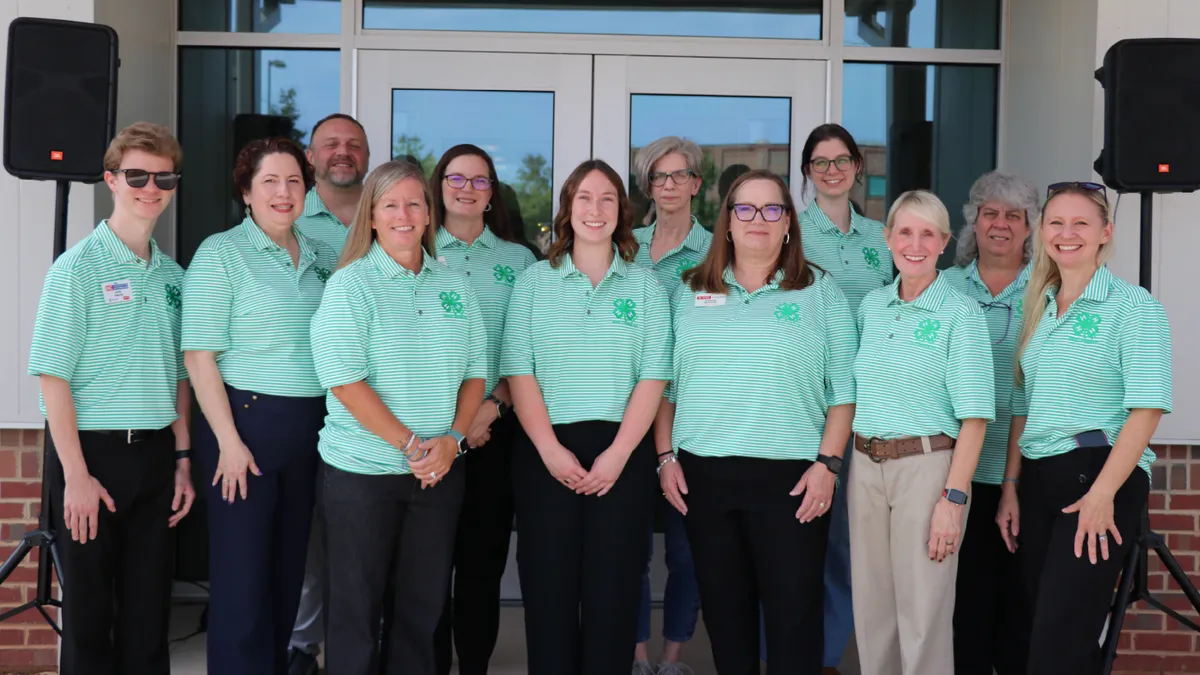 Twelve members of the North Carolina 4-H state team pose together outside the entrance to the CALS Extension Building, wearing matching green-and-white striped 4-H shirts.