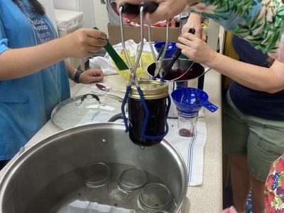 a hand is pulling a mason jar full of food out of a water bath canner