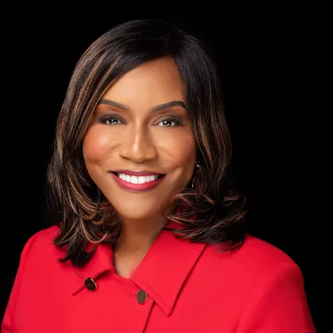 Portrait of Dr. Cassandra D. Caldwell smiling while wearing a bright red jacket against a black background.