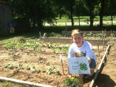 Boy in his garden posing for a picture beside his 4-H Mini gardening sign