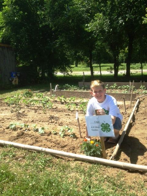 Boy in his garden posing for a picture beside his 4-H Mini gardening sign
