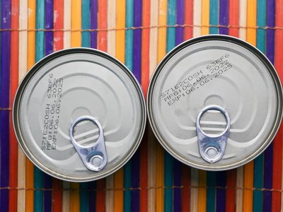 Two cans of food photographed from above showing expiration dates printed on the tops.