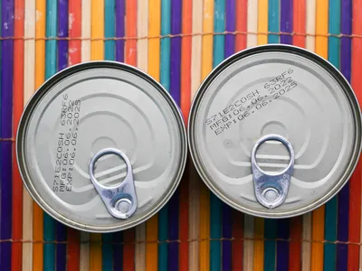 Two cans of food photographed from above showing expiration dates printed on the tops.