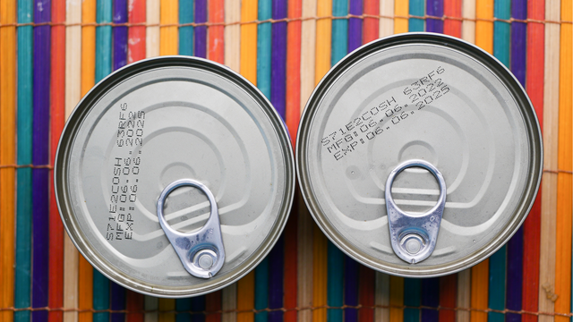 Two cans of food photographed from above showing expiration dates printed on the tops.