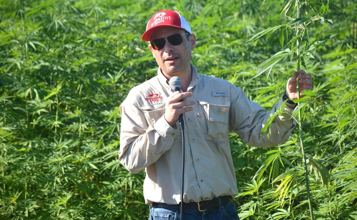NC State Extension expert David Suchoff holds a microphone and hemp plant while discussing the industry with a group of growers and industry stakeholders.