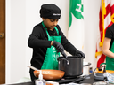 4-H member wearing a green apron and black chef hat stirring a pot.