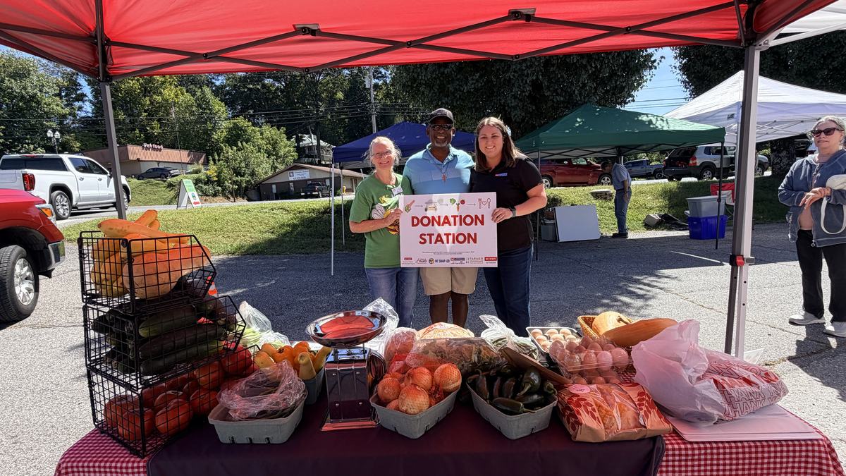 Donation Station at the Murphy Farmers Market with Volunteers holding Donation Station Sign in the background.