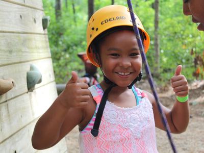 A young camper at NC State's Eastern 4-H Center in Columbia, North Carolina, gives a thumbs up while preparing for the zip line.