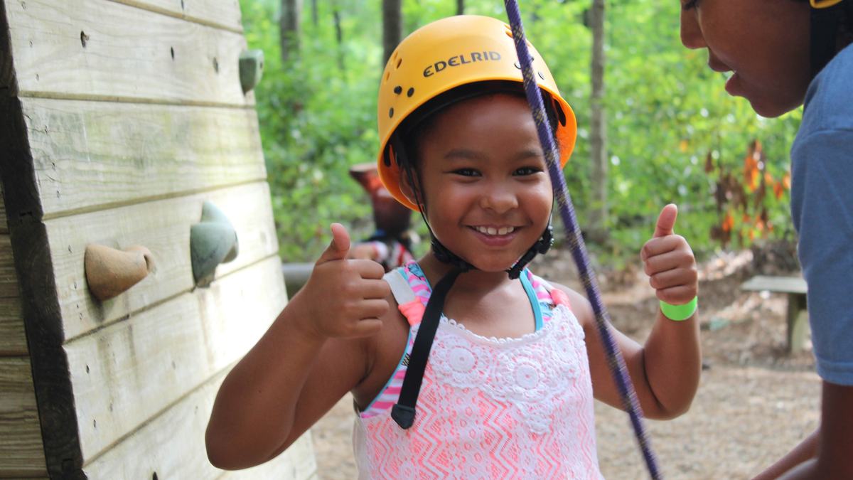 A young camper at NC State's Eastern 4-H Center in Columbia, North Carolina, gives a thumbs up while preparing for the zip line.