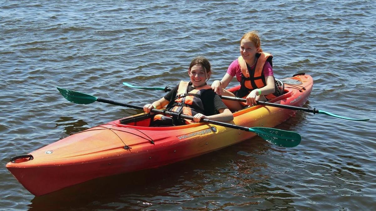 Two young girls paddle a tandem kayak