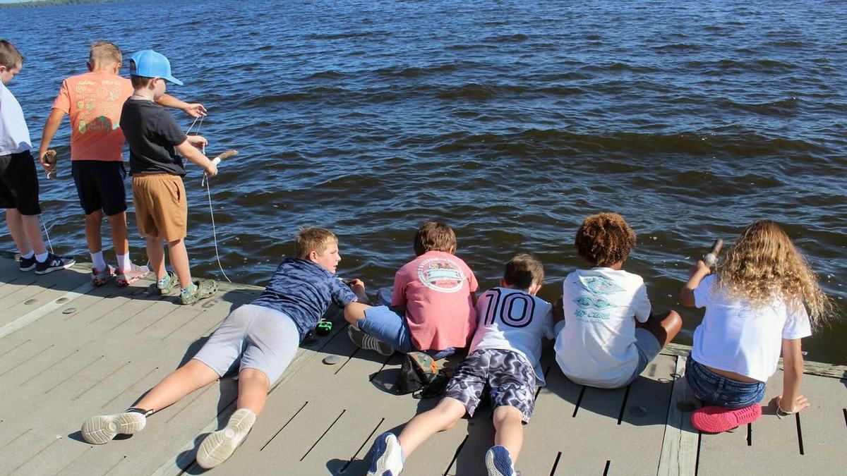Boys and girls standing, kneeling and laying on a dock dropping baited string into the water