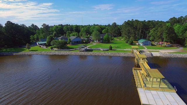 An overhead view of the NC State Extension 4-H center on the Albemarle Sound looking toward the shore with a dock extending into the water in the foreground and camp buildings and trees in the background