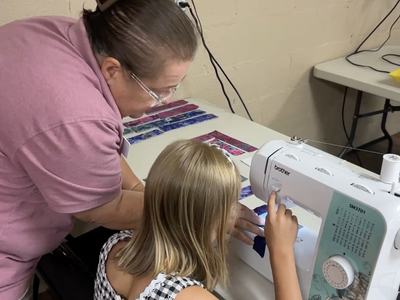 Girl sewing with an adult helper.