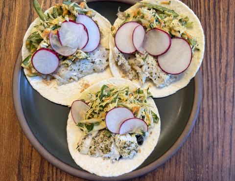 Plate with fish tacos topped with slaw and radishes.
