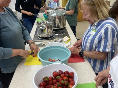 group of people in a kitchen prepping strawberries to can strawberry jam