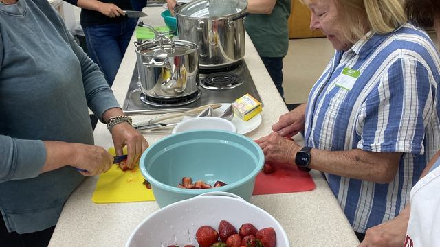 group of people in a kitchen prepping strawberries to can strawberry jam