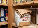 An AI generated image of pantry moths by a bag of flour in a pantry.
