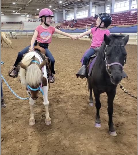 Two girls riding horses and holding hands at a horsemanship clinic.
