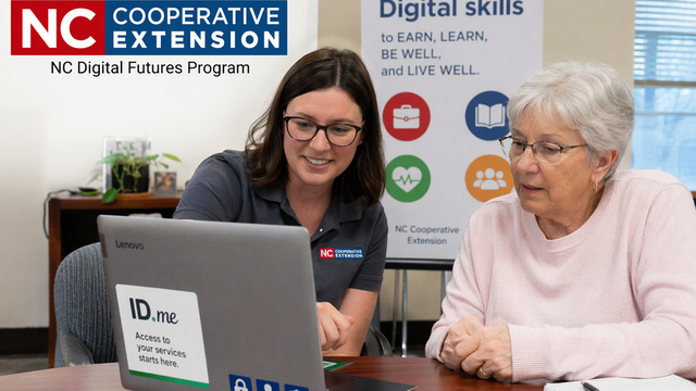 A staff member helps an older woman at a laptop labeled "ID.me." NC Cooperative Extension logo and a "Digital skills" poster are visible, suggesting a digital skills training session.