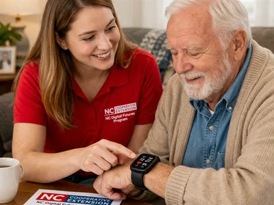 A Digital Skills Educator sits beside an older man in his home, showing him how to use a smartwatch to monitor important health information.