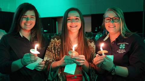 Three 4-H members stand side by side holding lit candles during the annual Honor Club tapping ceremony at 4-H Congress.