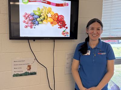 Paige wearing an EFNEP polo standing next to a tv screen projecting a youth lesson.