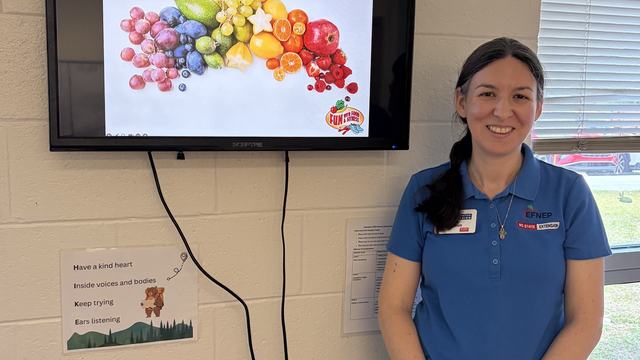 Paige wearing an EFNEP polo standing next to a tv screen projecting a youth lesson.