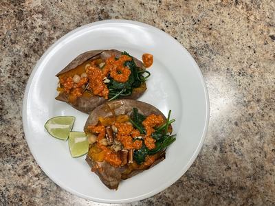 Cooked sweet potatoes with chickpeas, spinach, and red pepper sauce with two pieces of lime all on a white dinner plate on a kitchen counter.