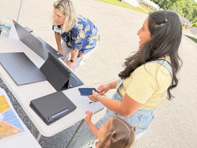 A woman and a child with a table holding computers.  Another woman is looking at a computer screen.