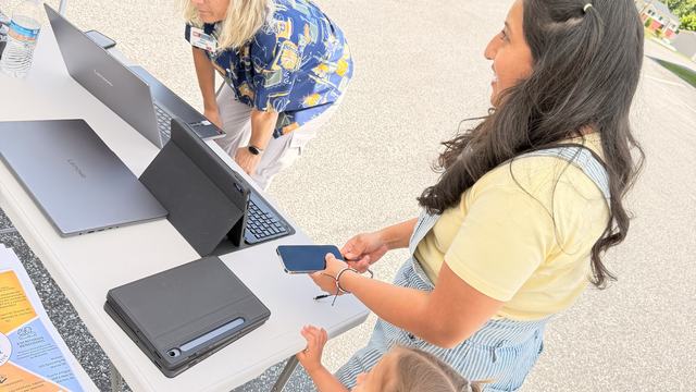 A woman and a child with a table holding computers.  Another woman is looking at a computer screen.