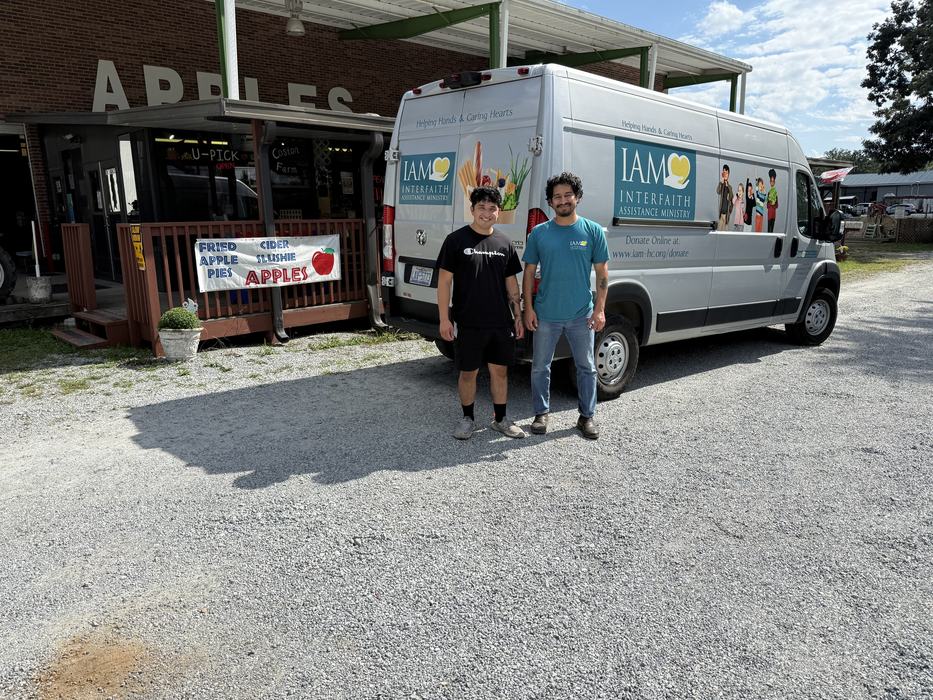 Two men standing in front of an Interfaith Assistance Ministry van outside an apple farm shop.