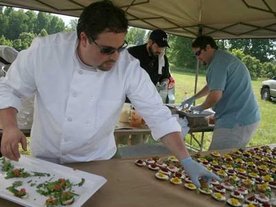 Chef in white jacket arranging bite-sized appetizers on table under outdoor tent