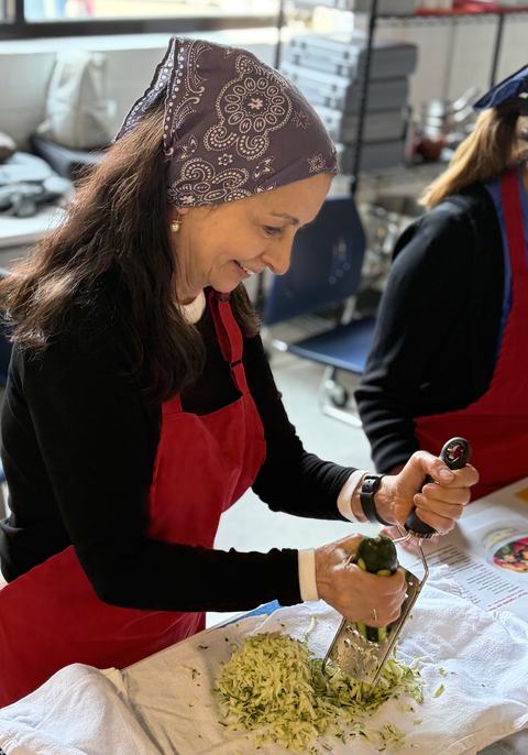 staff wearing apron in kitchen while shredding zucchini