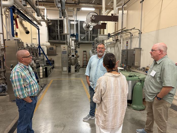 Four people discuss textile machinery during a tour of an industrial facility.