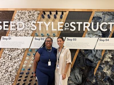 Two people stand in front of a textile recycling display featuring cotton, thread and denim.