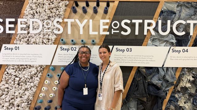 Two people stand in front of a textile recycling display featuring cotton, thread and denim.