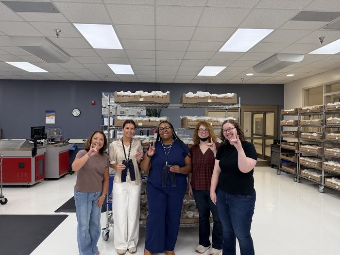 Five people pose in a textile facility surrounded by cotton samples and equipment.