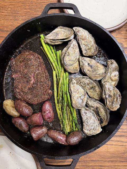 Oysters with asparagus, potatoes, and steak in a cast iron skillet.