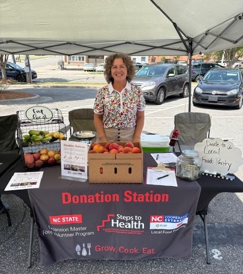 FCS Agent Andrea Sherill standing behind the Donation Station table where she is collecting food and monetary donations to support local farmers and food security in her community.