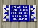 Photo of a sign on an exterior wall. Text reads:
Hiwasse Dam Senior Center Nutrition Site - M-F 8AM-1PM - 828-644-0400