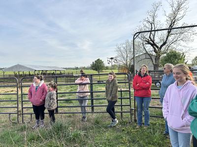 Students, parents, and livestock agent Ms. Kristi standing in a fenced livestock area during a 4-H dairy project visit
