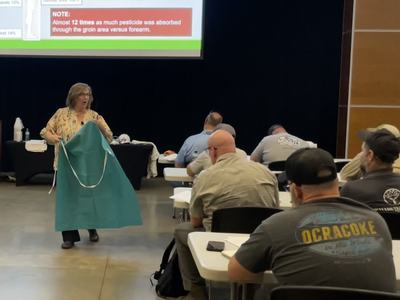 A female instructor showing a PPE apron to pesticide applicators attending a Pesticide Safety School.