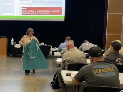 A female instructor showing a PPE apron to pesticide applicators attending a Pesticide Safety School.
