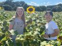 Two girls stand together in a field with a blooming sunflower.