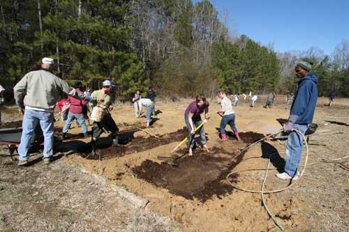 Volunteers digging and spreading soil in a field using shovels, rakes, and hoses.