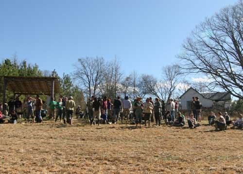 Large group of people gathered on dry field near pavilion and small white building