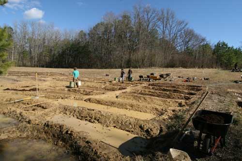 Field excavation trenches with workers, wheelbarrows, and tools