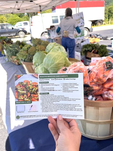 Recipe for roasted carrots and broccoli in front of fresh produce at a local free market