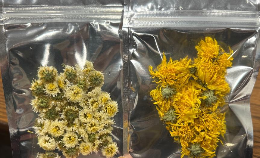 Two sealed packages, side by side, containing dried yellow and light yellow flowers.